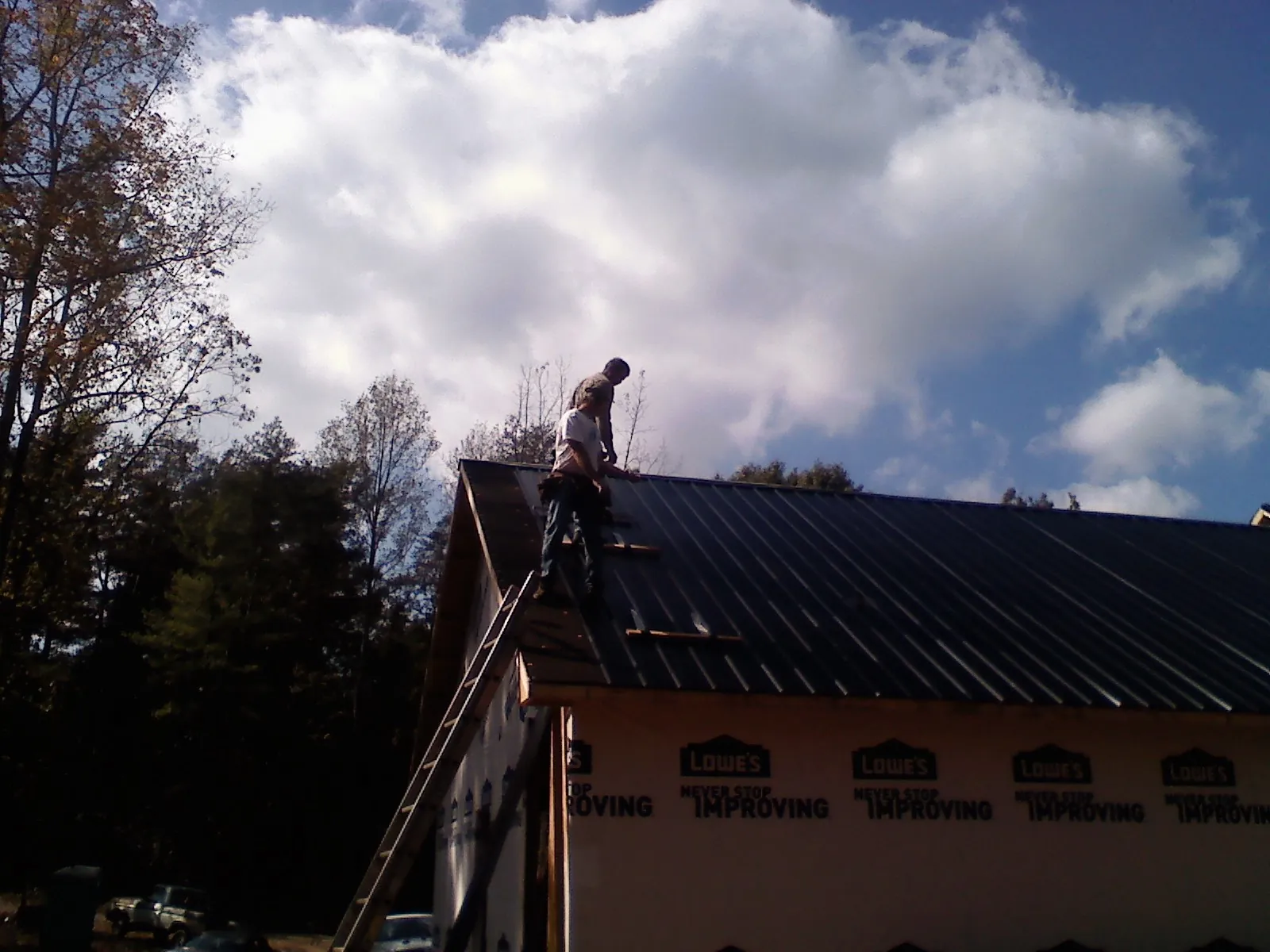 Roofer fastening dark metal panels high against a cloudy sky, from a Roof Inspection job in Olympia